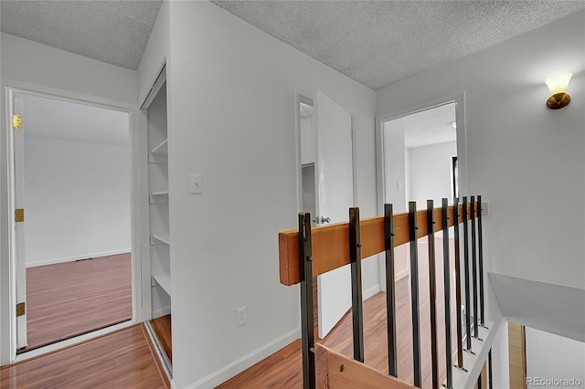 corridor with a textured ceiling, baseboards, and wood finished floors