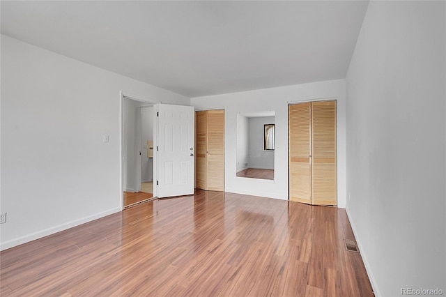 unfurnished bedroom featuring baseboards, visible vents, two closets, and light wood-style floors