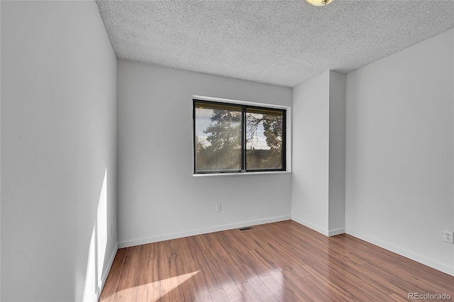 empty room with visible vents, baseboards, a textured ceiling, and wood finished floors