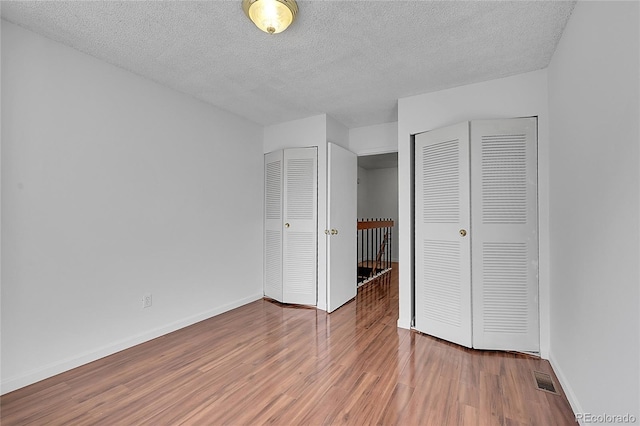 unfurnished bedroom with visible vents, two closets, a textured ceiling, wood finished floors, and baseboards