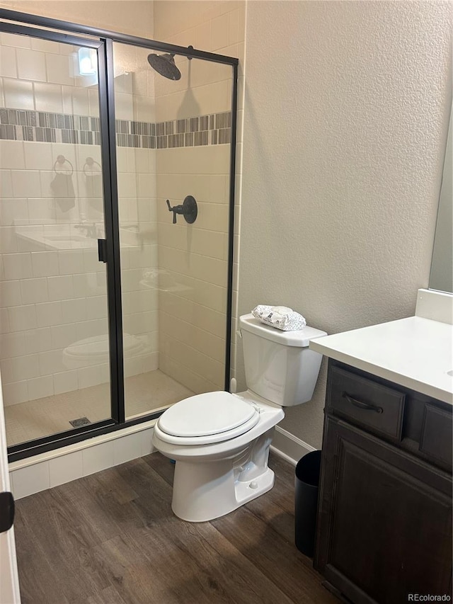 bathroom with wood finished floors, toilet, vanity, a shower stall, and a textured wall