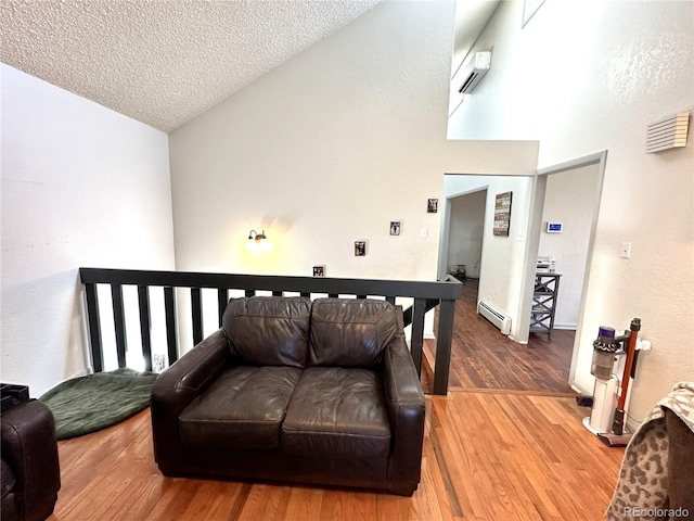 living room with a textured ceiling, vaulted ceiling, a baseboard radiator, an AC wall unit, and hardwood / wood-style floors