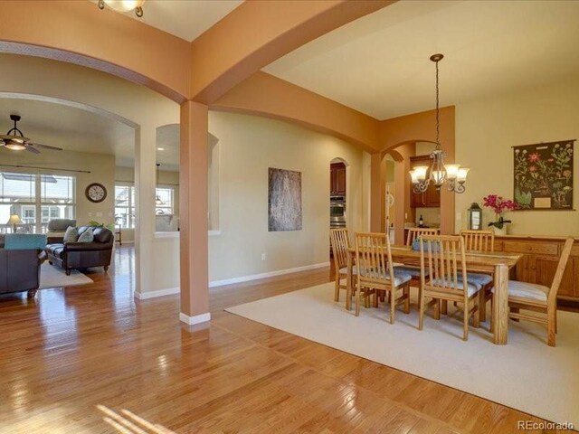 dining room featuring ceiling fan with notable chandelier, light wood-type flooring, arched walkways, and baseboards