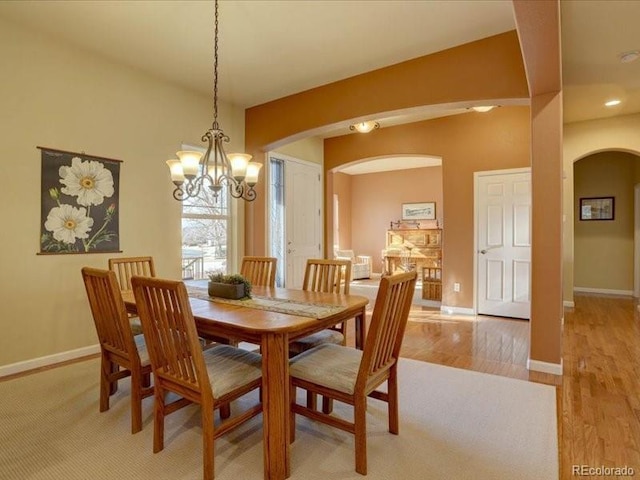 dining space with baseboards, arched walkways, and light wood-style flooring