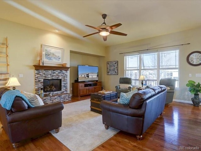 living area featuring ceiling fan, a fireplace, wood finished floors, and baseboards