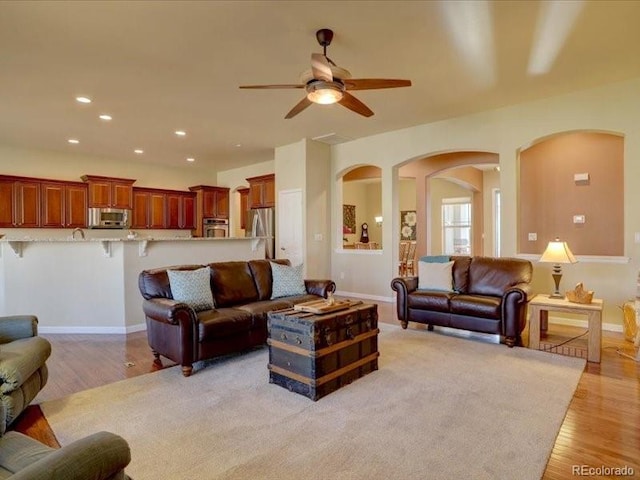 living room featuring baseboards, ceiling fan, light wood finished floors, and recessed lighting