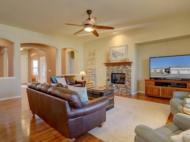 living room featuring ceiling fan, a stone fireplace, baseboards, and wood finished floors