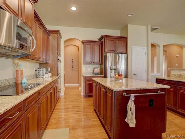 kitchen with arched walkways, light wood-style flooring, recessed lighting, appliances with stainless steel finishes, and a center island