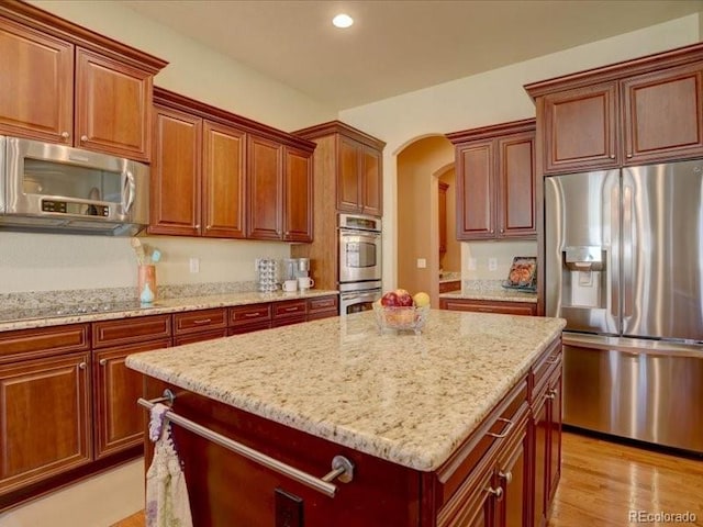 kitchen featuring arched walkways, light stone counters, a kitchen island, light wood-style floors, and appliances with stainless steel finishes