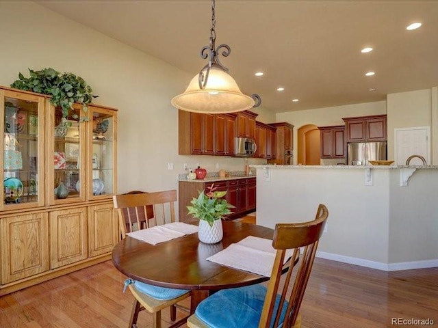 dining room featuring light wood finished floors, baseboards, arched walkways, and recessed lighting