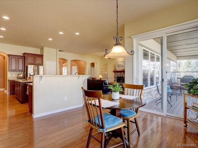 dining area featuring light wood-style floors, recessed lighting, arched walkways, and a stone fireplace