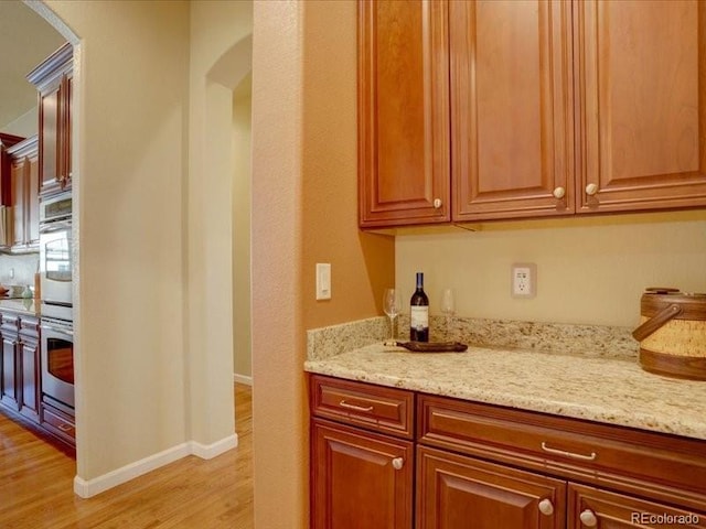 kitchen featuring light wood-style flooring, light stone counters, brown cabinets, and baseboards