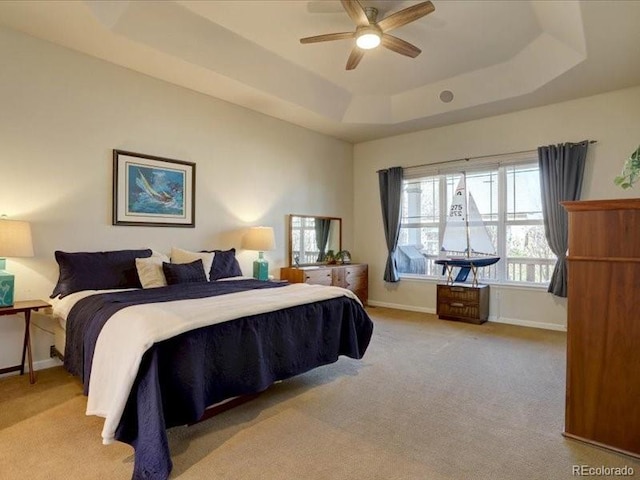 carpeted bedroom featuring a ceiling fan, a tray ceiling, and baseboards