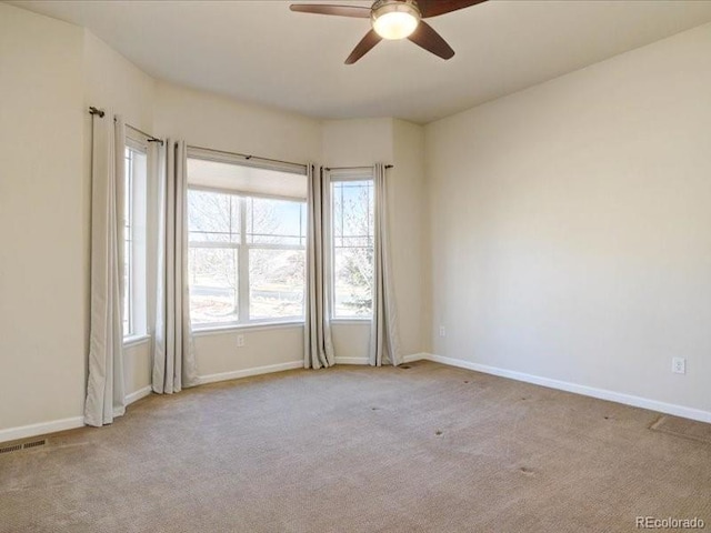 carpeted spare room featuring a ceiling fan, visible vents, and baseboards