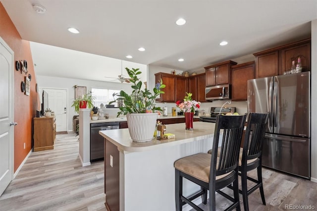 kitchen featuring appliances with stainless steel finishes, light countertops, light wood-style floors, a kitchen bar, and recessed lighting