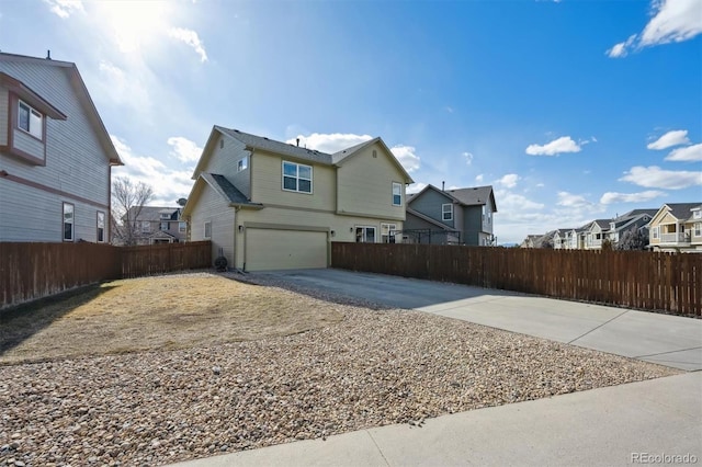 view of side of home featuring concrete driveway, an attached garage, fence, and a residential view