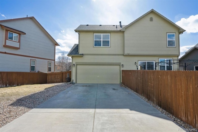 rear view of property with a garage, fence, and driveway