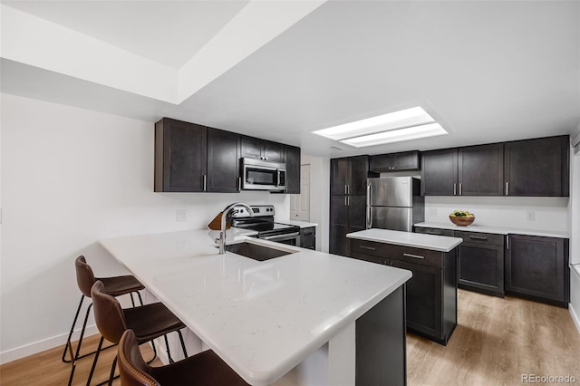 kitchen featuring a breakfast bar area, a peninsula, light countertops, appliances with stainless steel finishes, and light wood-type flooring