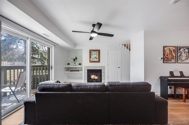 living room with a ceiling fan, visible vents, light wood-style flooring, and a tiled fireplace