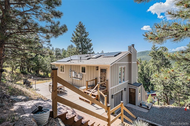 32783 Lodgepole Cir, Evergreen, CO 80439 - rear view of property with solar panels, a wooden deck, a chimney, board and batten siding, and roof with shingles