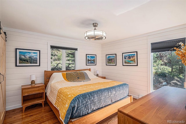 32783 Lodgepole Cir, Evergreen, CO 80439 - bedroom featuring multiple windows, hardwood / wood-style floors, wood walls, and a barn door