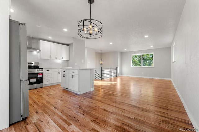 kitchen featuring white cabinets, a notable chandelier, light wood-type flooring, wall chimney exhaust hood, and stainless steel appliances