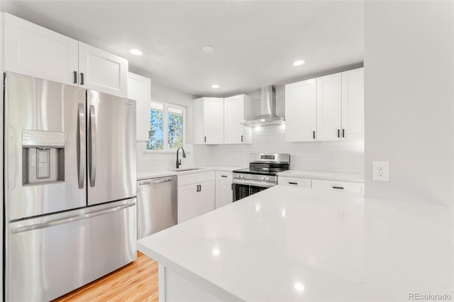 kitchen with wall chimney exhaust hood, white cabinetry, stainless steel appliances, and light wood-type flooring