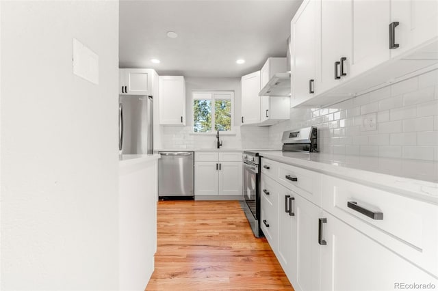 kitchen featuring white cabinetry, wall chimney range hood, stainless steel appliances, and light hardwood / wood-style floors