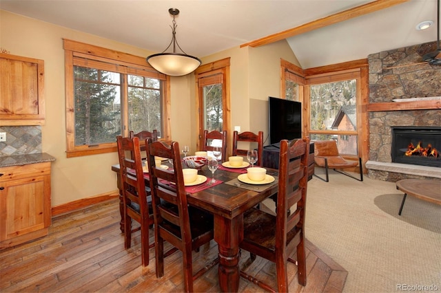 dining area featuring lofted ceiling, plenty of natural light, a fireplace, and light wood-style flooring