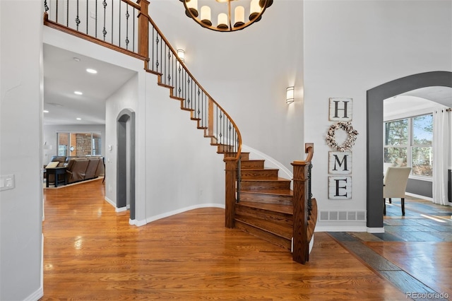 stairs with a notable chandelier, hardwood / wood-style floors, and a high ceiling