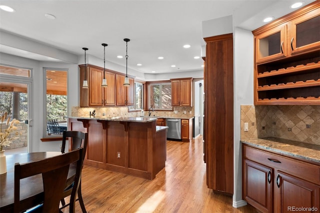 kitchen featuring pendant lighting, dishwasher, light stone counters, and a breakfast bar area