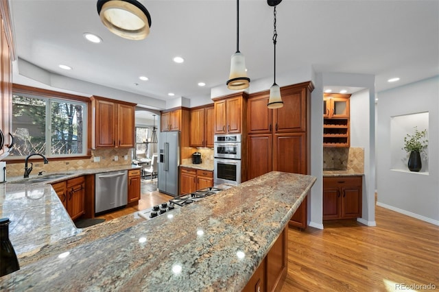 kitchen featuring appliances with stainless steel finishes, sink, pendant lighting, and light stone counters