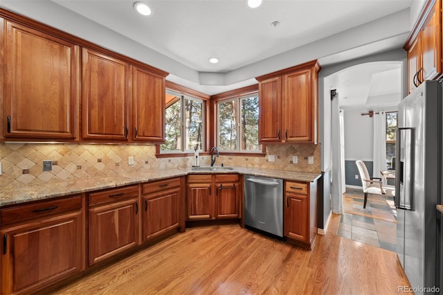 kitchen featuring sink, light hardwood / wood-style flooring, appliances with stainless steel finishes, light stone countertops, and decorative backsplash