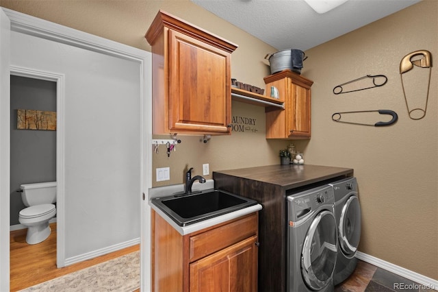 laundry room with separate washer and dryer, sink, light hardwood / wood-style flooring, and cabinets