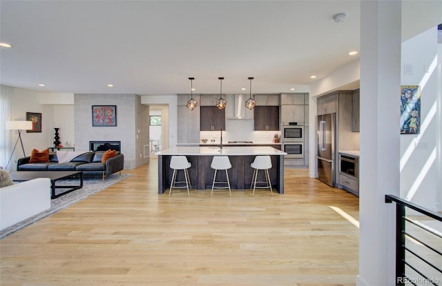 kitchen featuring a center island with sink, light wood-type flooring, appliances with stainless steel finishes, a large fireplace, and a kitchen bar