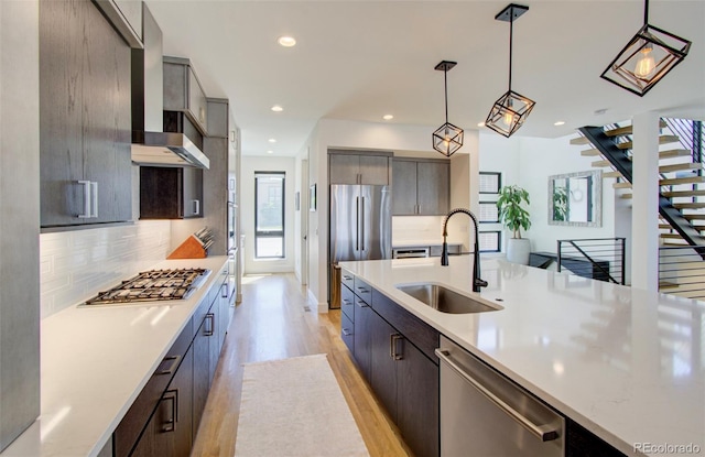 kitchen featuring sink, wall chimney exhaust hood, stainless steel appliances, light hardwood / wood-style flooring, and pendant lighting