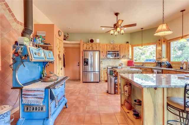 kitchen featuring ceiling fan, light tile patterned flooring, hanging light fixtures, appliances with stainless steel finishes, and a kitchen bar