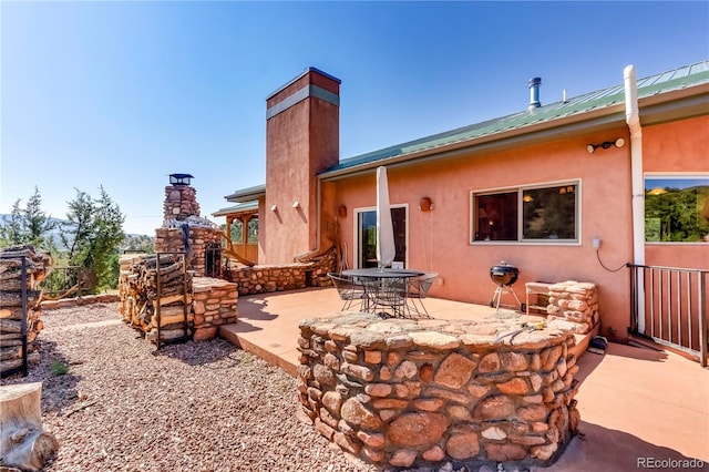 rear view of property featuring metal roof, a patio, a chimney, and stucco siding