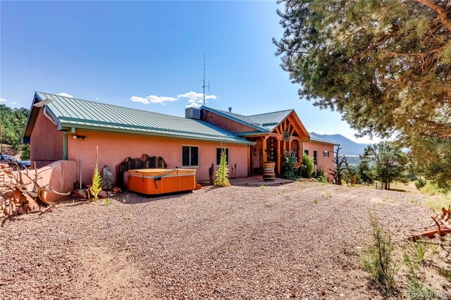 rear view of house featuring a hot tub, central AC, stucco siding, metal roof, and a patio area