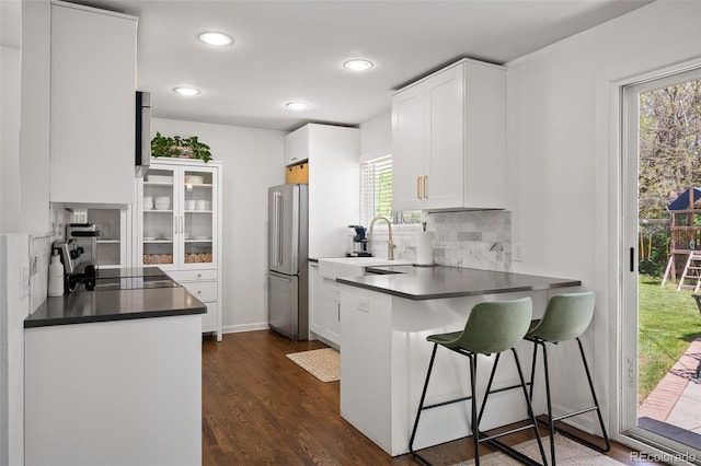 986 S Jersey St, Denver, CO 80224 - kitchen featuring freestanding refrigerator, decorative backsplash, dark countertops, white cabinetry, and a kitchen bar