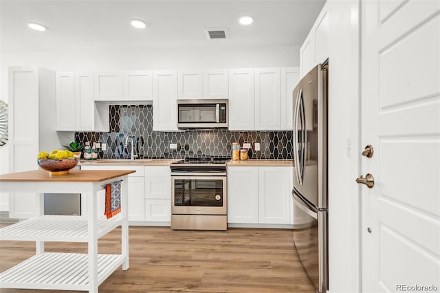 kitchen with appliances with stainless steel finishes, tasteful backsplash, sink, light hardwood / wood-style flooring, and white cabinetry