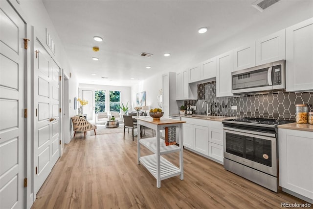 kitchen featuring white cabinetry, tasteful backsplash, appliances with stainless steel finishes, and light hardwood / wood-style flooring