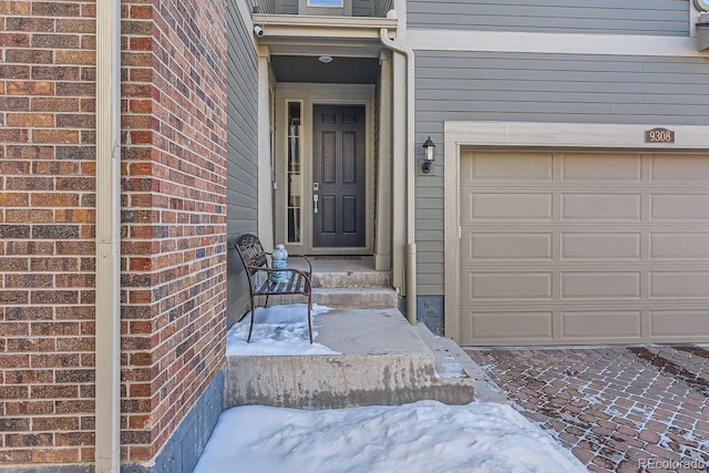 snow covered property entrance with a garage