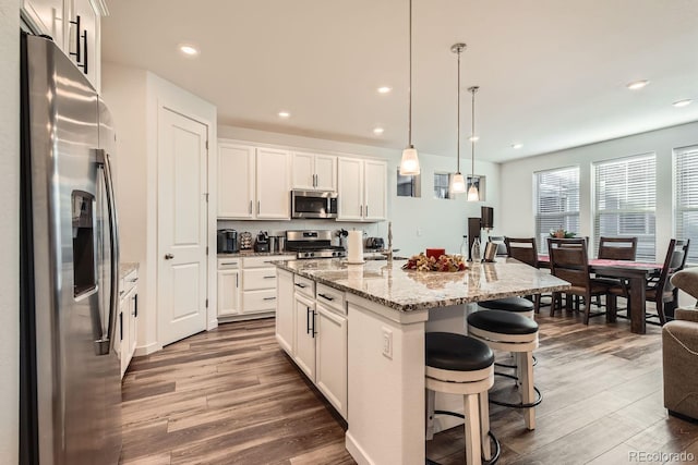 kitchen with stainless steel appliances, an island with sink, white cabinets, and decorative light fixtures