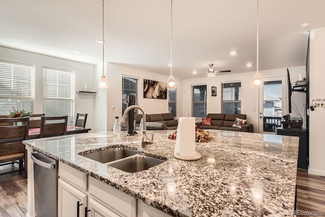 kitchen featuring sink, light stone counters, decorative light fixtures, a center island with sink, and white cabinets