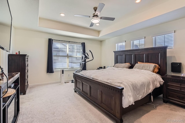 carpeted bedroom featuring a raised ceiling, ceiling fan, and multiple windows