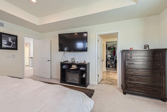 bedroom featuring a raised ceiling, a spacious closet, and light colored carpet