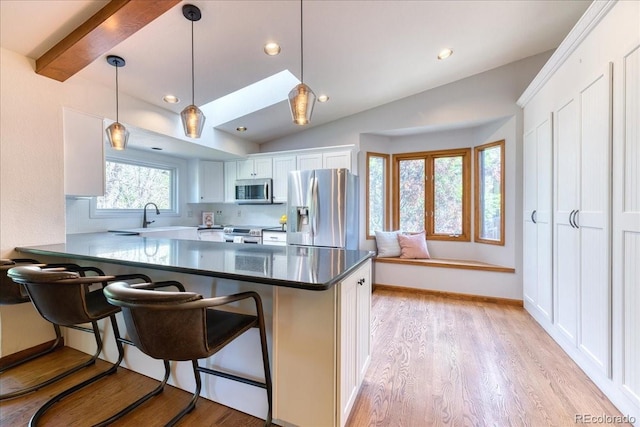 kitchen featuring appliances with stainless steel finishes, vaulted ceiling, light wood-style floors, a peninsula, and a kitchen breakfast bar
