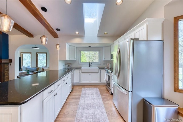 kitchen with appliances with stainless steel finishes, a sink, white cabinets, light wood finished floors, and a peninsula