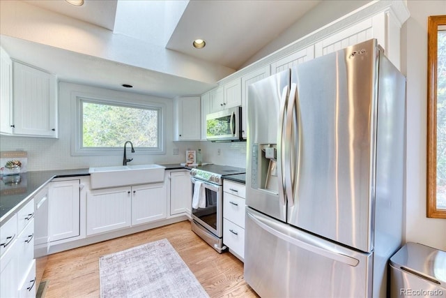kitchen with appliances with stainless steel finishes, a sink, white cabinets, backsplash, and light wood finished floors